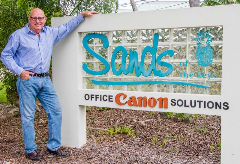 Founder George Sands standing beside the Sands of the Keys sign at the Islamorada office.